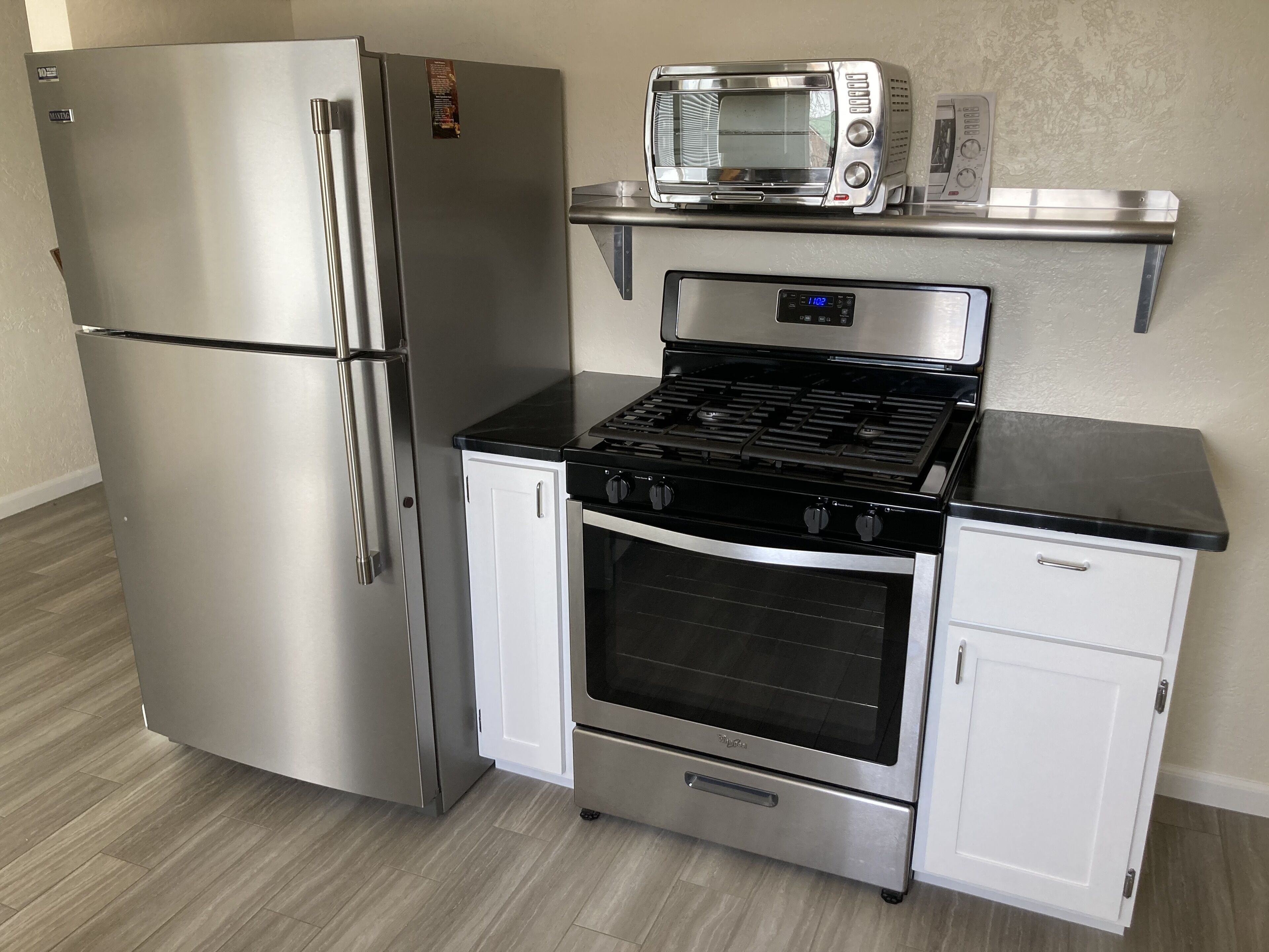 Una cocina compacta con refrigerador de acero inoxidable, microondas y estufa con un gabinete blanco debajo.