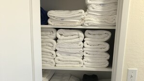 A closet with neatly folded towels in white, gray, and black, and a basket of folded clothes.