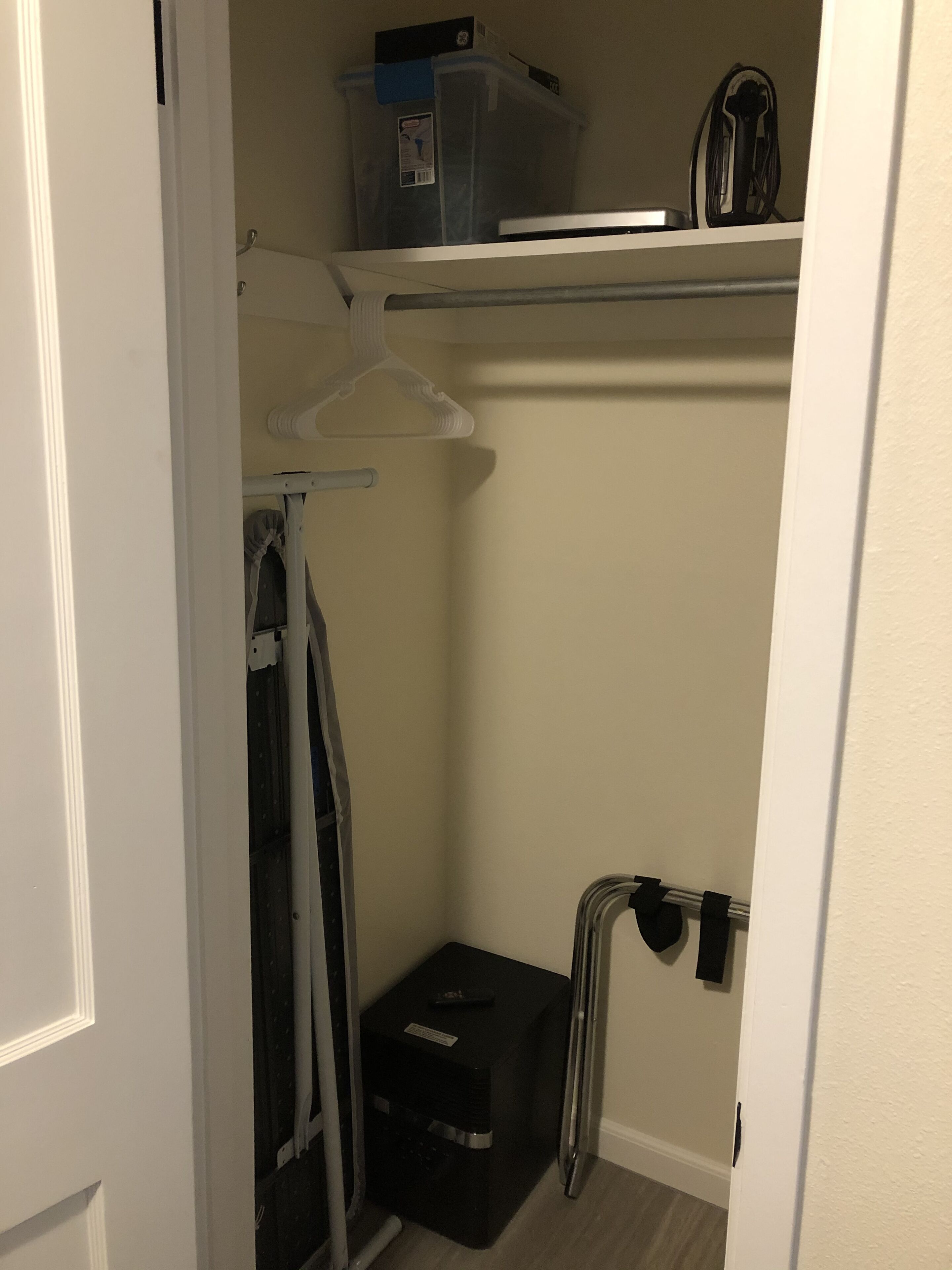 A small walk-in closet with a hanging rack, a storage box, and a shelf with a few items.
