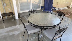 A round metal table with four chairs, a blue folding chair, and a metal bench.
