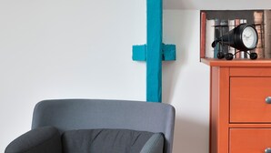 Une chaise avec un siège en tissu gris et des pieds en métal noir, placée à côté d’une commode en bois dotée de tiroirs et sur laquelle se trouve une horloge.