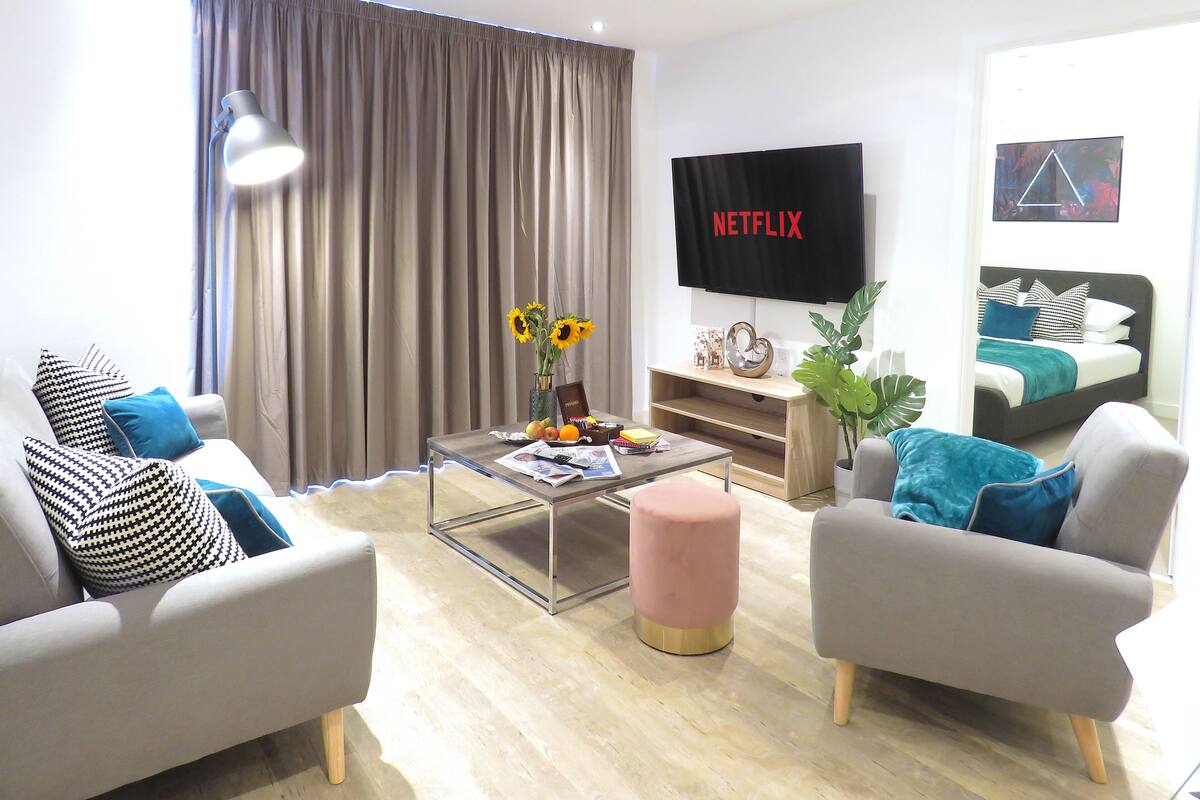 Een moderne woonkamer met een bank, fauteuils, een salontafel en een aan de muur bevestigde televisie.