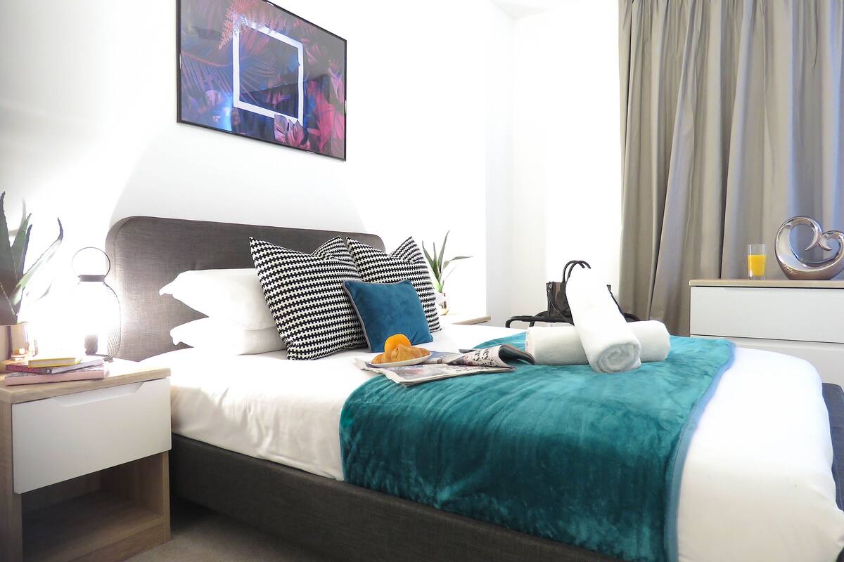 Een keurig ingerichte hotelkamer met een bed, nachtkastjes, een plant in pot en een schilderij aan de muur.