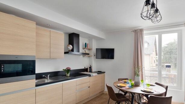 A modern kitchen with wooden cabinets, a black stove, and a dining area with a table and chairs.