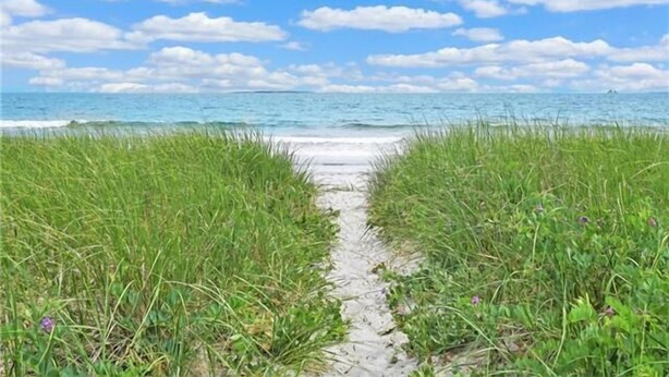 Een pad dat naar een strand leidt, met begroeide oevers en een heldere lucht.