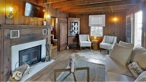 Een gezellig interieur van een chalet met een open haard, houten wanden, een aan de muur bevestigde televisie en een comfortabele zithoek met een bank en stoelen.
