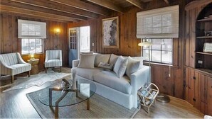 Een gezellig interieur van een chalet met houten plafond, een bank, twee fauteuils, een glazen salontafel en een open haard.