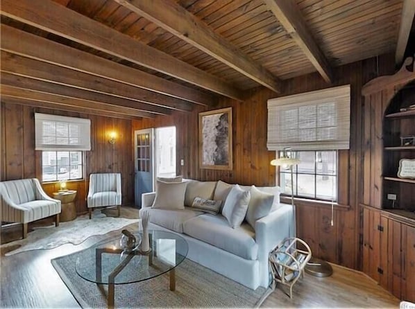 L’intérieur chaleureux d’un chalet avec un plafond en bois, un canapé, deux fauteuils, une table basse en verre et une cheminée.