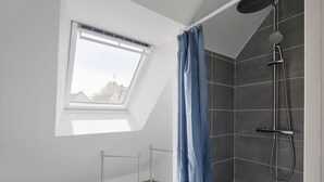 A modern shower with a handheld showerhead, a blue shower curtain, and a skylight window.