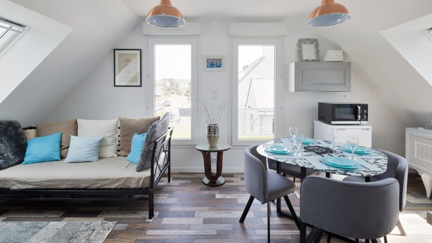 A loft-style room with a loft bed, dining table with chairs, and a kitchen area.