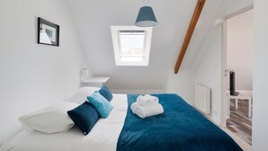 A bedroom with a bed, pillows, a blue blanket, a window, and a ceiling light.