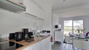 A modern kitchen with a built-in stove, coffee maker, and a small dining area with a glass table and chairs. - Le Repos- À 300 m de la plage, St Lunaire (Saint-Lunaire)