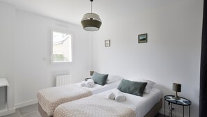 A modern bedroom with two beds, a bedside table, a lamp, and a window. - Le Repos- À 300 m de la plage, St Lunaire (Saint-Lunaire)