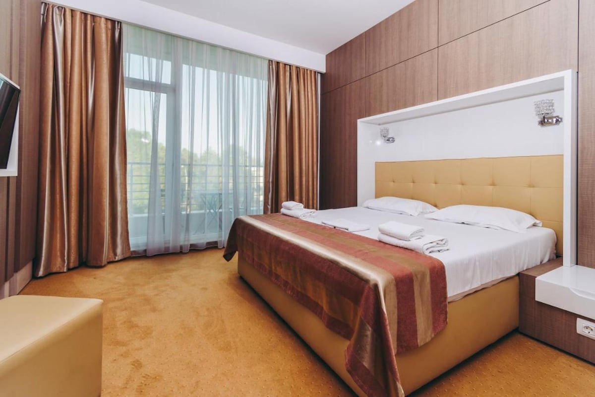 A hotel room with a large bed, a bedside table, a TV, and a window with curtains.