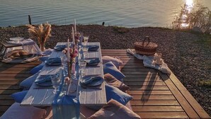 Eine Holzterrasse mit gedecktem Tisch, mit Blick auf ruhiges Wasser.