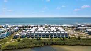 Een kusthotel met meerdere gebouwen in een rasterpatroon, met uitzicht op het strand en een klein waterlichaam op de voorgrond.
