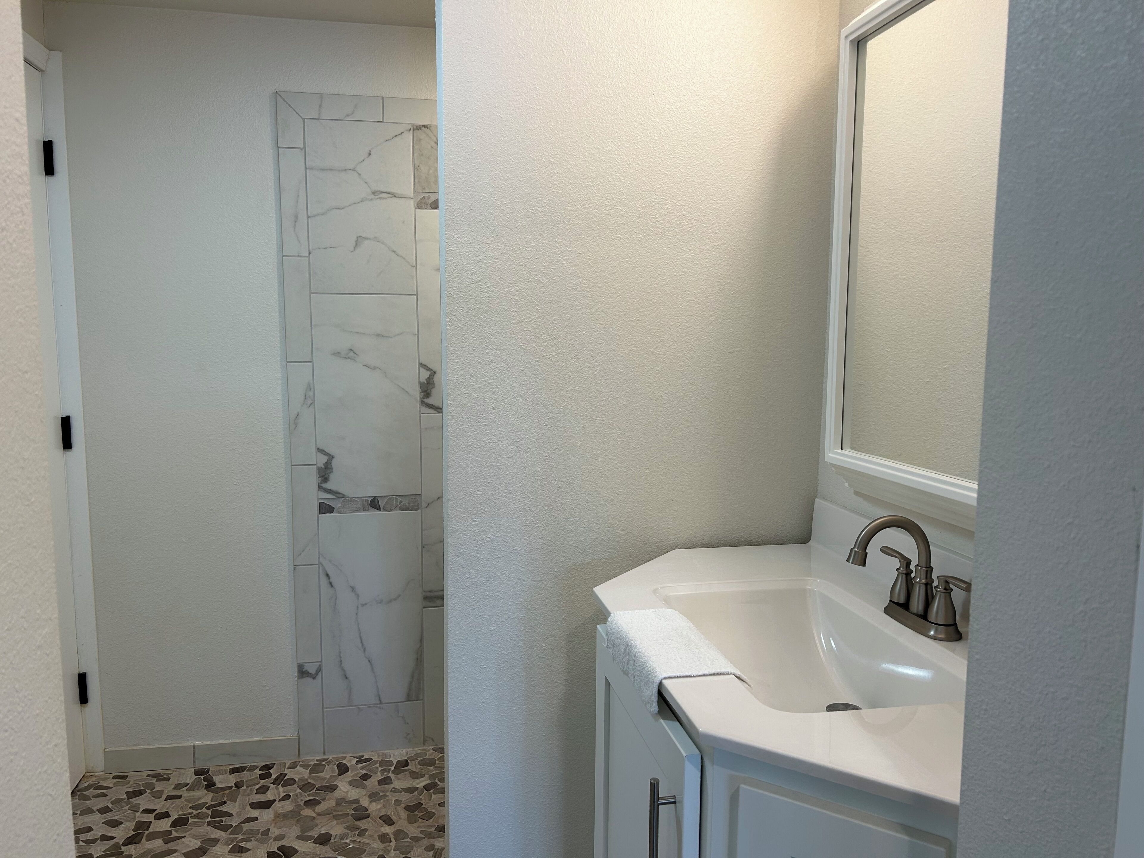 Une salle de bain avec un lavabo blanc, un miroir et une douche aux carreaux de marbre.