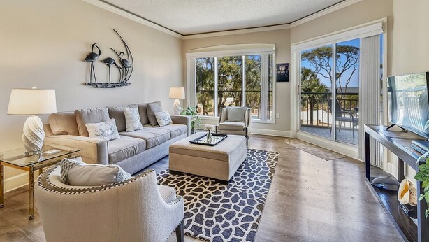 A spacious living room with a sofa, armchair, and ottoman, a glass coffee table, and a television. - 1BR Villa w/ Private Balcony Overlooking Beach (Hilton Head Island)
