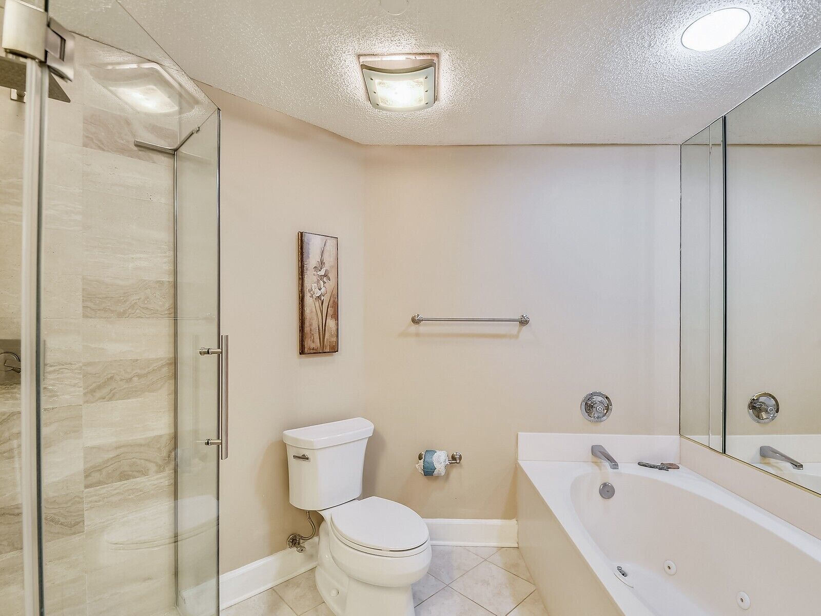 A modern bathroom with a glass shower enclosure, a toilet, a bathtub, and a handrail.