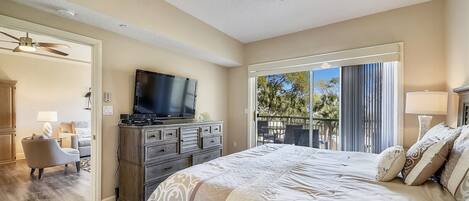 Un dormitorio amplio con una cama grande, televisión de pantalla plana, ventilador de techo y balcón con mobiliario exterior.