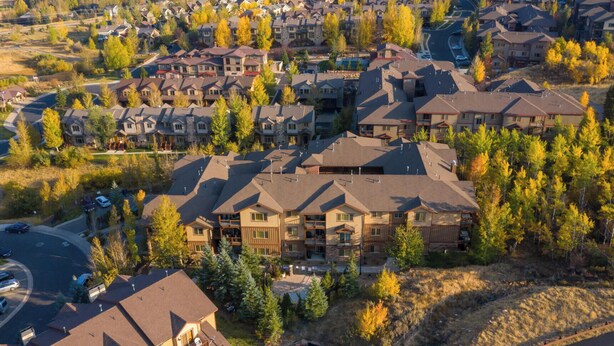 A residential area with multiple two-story houses, a winding road, and a mix of deciduous trees.