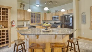 A kitchen with wooden cabinets, granite countertops, a central island with stools, stainless steel appliances, and pendant lighting.