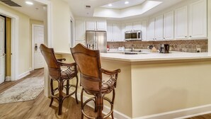 Una cocina moderna con gabinetes blancos, una isla grande con taburetes de bar, electrodomésticos de acero inoxidable y un salpicadero de azulejos.
