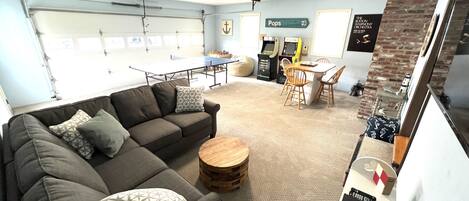 A modern living room with a sectional sofa, a ping pong table, and a dining area with chairs.