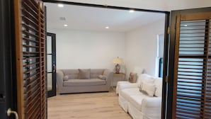 A room with a grey sofa, a white sofa, a small table with a lamp, and wooden blinds. - Coastal modern home (Newport Beach)
