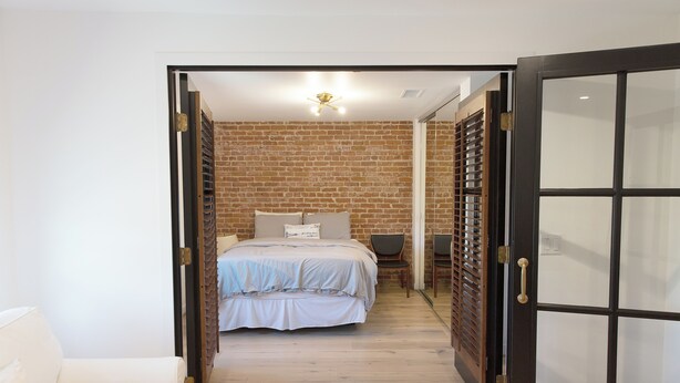 A bedroom with a brick wall, a bed with a light-colored duvet, and a wooden floor. - Coastal modern home (Newport Beach)
