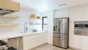 A modern kitchen with white cabinetry, stainless steel appliances, and a wooden countertop. - Coastal modern home (Newport Beach)