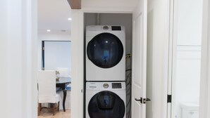 A laundry room with two stacked washing machines, a wooden floor, and a white door leading to a bathroom. - Coastal modern home (Newport Beach)