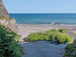 Une plage avec une structure en pierre, une eau d’un bleu limpide et quelques plantes.