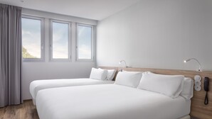 A modern hotel room with two single beds, a wooden headboard, bedside lamps, a phone, and a window with curtains. - B&B Hotel Lisboa Aeroporto (Loures)