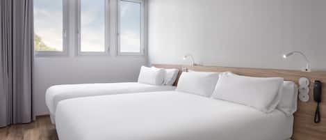 A modern hotel room with two single beds, a wooden headboard, bedside lamps, a phone, and a window with curtains.