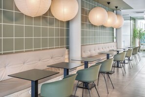 Un interior de restaurante moderno con cabinas acolchadas, sillas verdes e iluminación colgante.