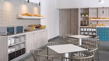 A modern kitchen with a built-in oven, a coffee machine, and a fruit display. There are white cabinets, grey tiles, and a blue tiled wall.