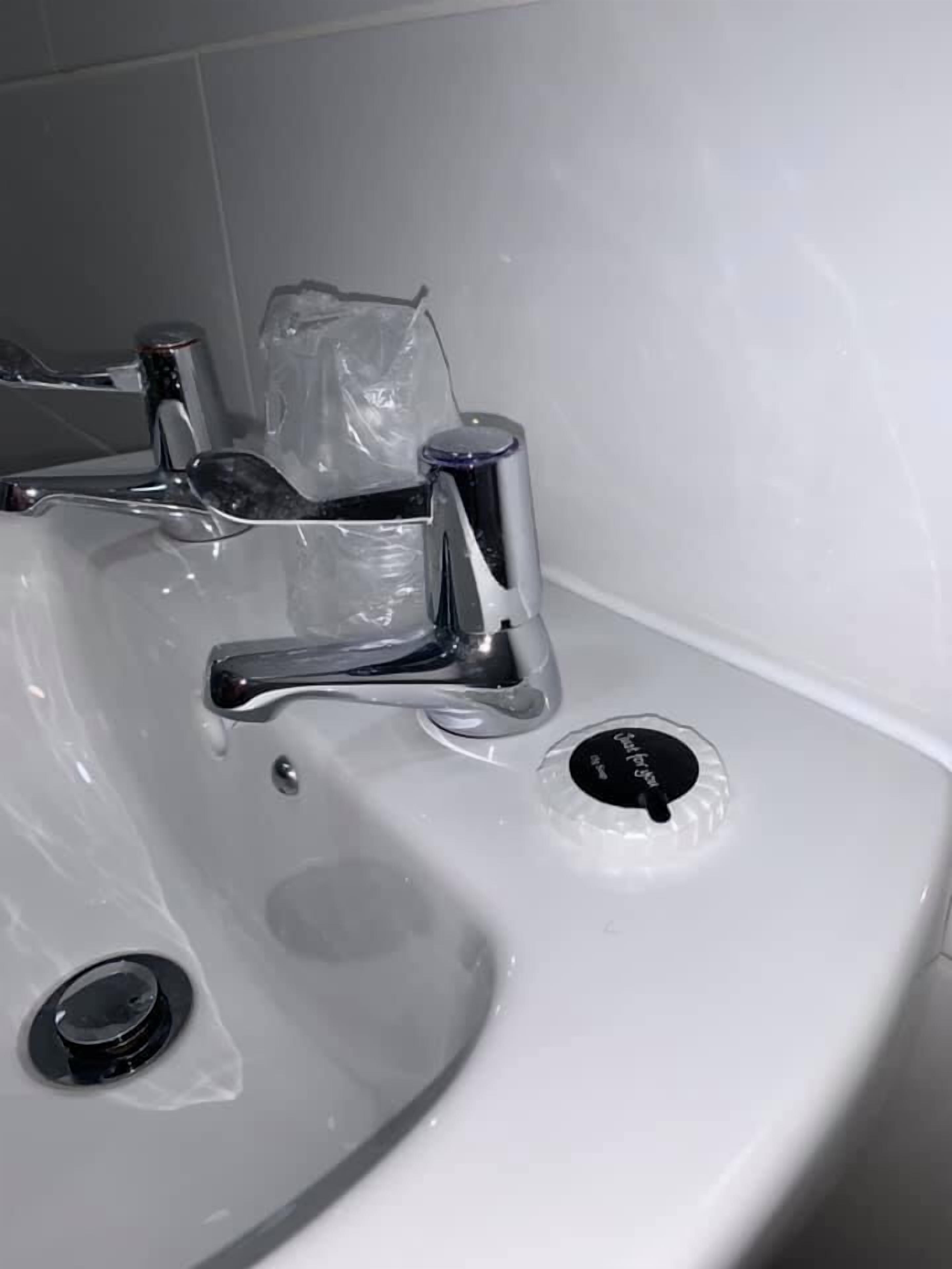 Un lavamanos blanco con grifo cromado, dispensador de jabón y desagüe.