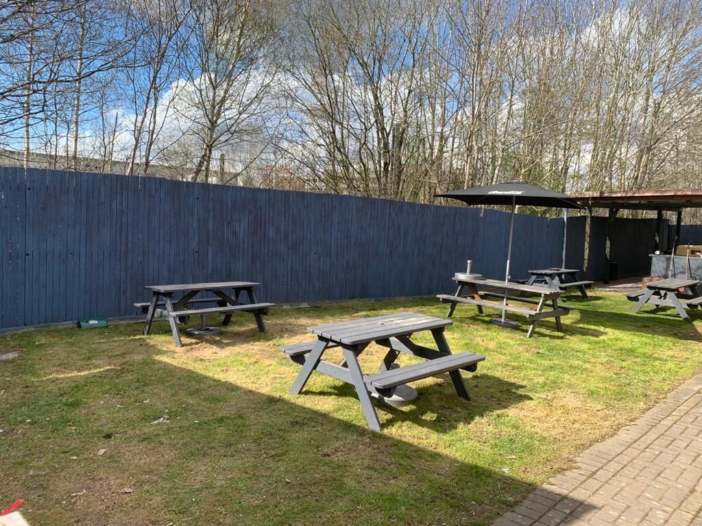 Un jardin avec des tables de pique-nique et un espace barbecue.