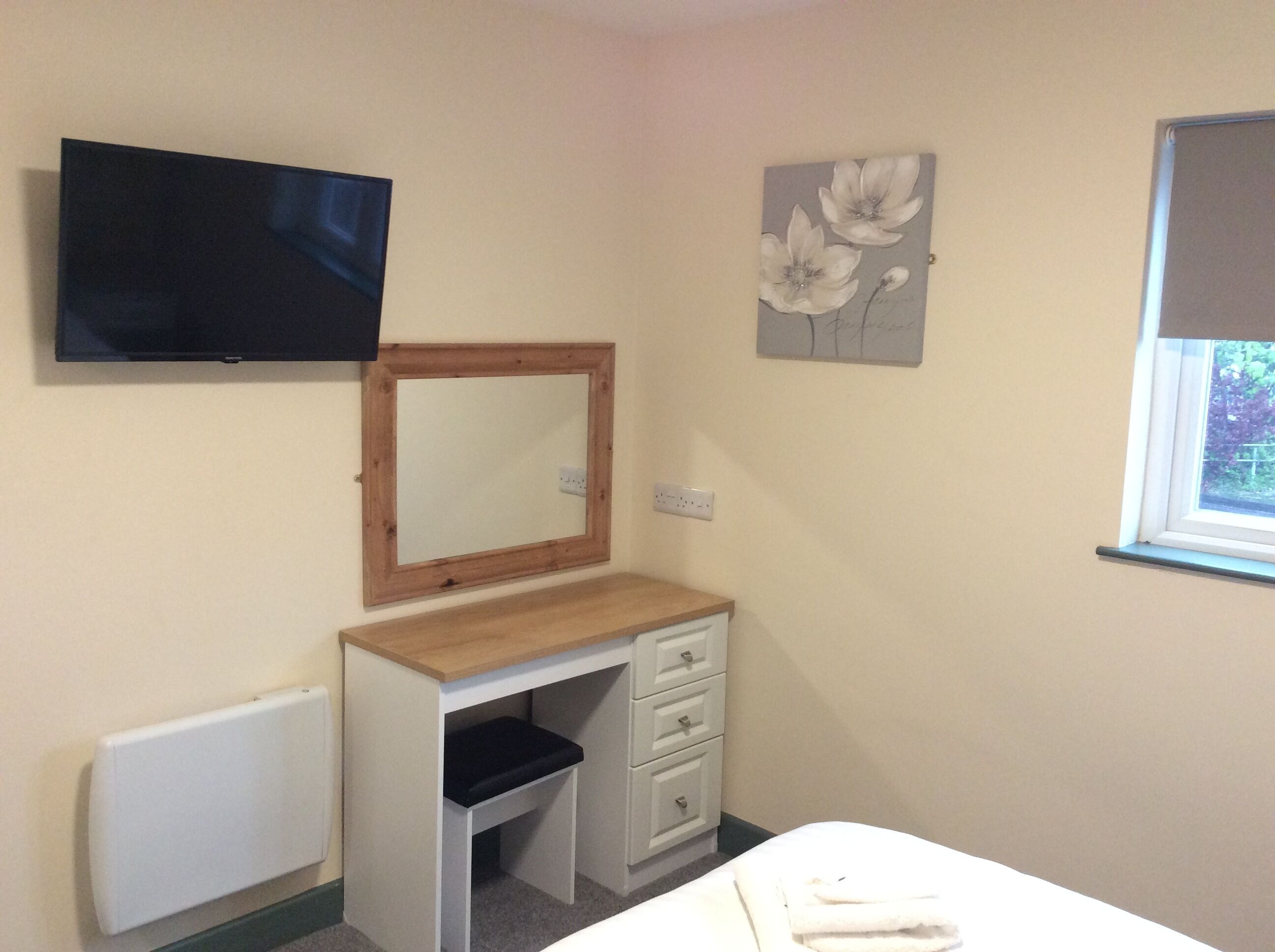 A bedroom with a bed, a dresser, a mirror, a flat-screen TV, and a window.