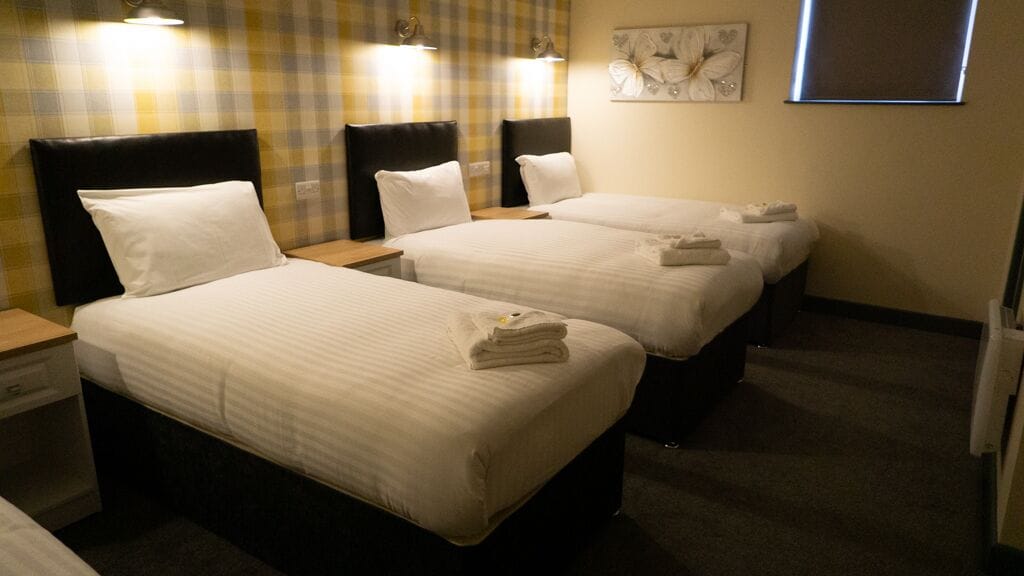 Een hotelkamer met twee eenpersoonsbedden, elk voorzien van een hoofdeinde, nachtkastjes en handdoeken.