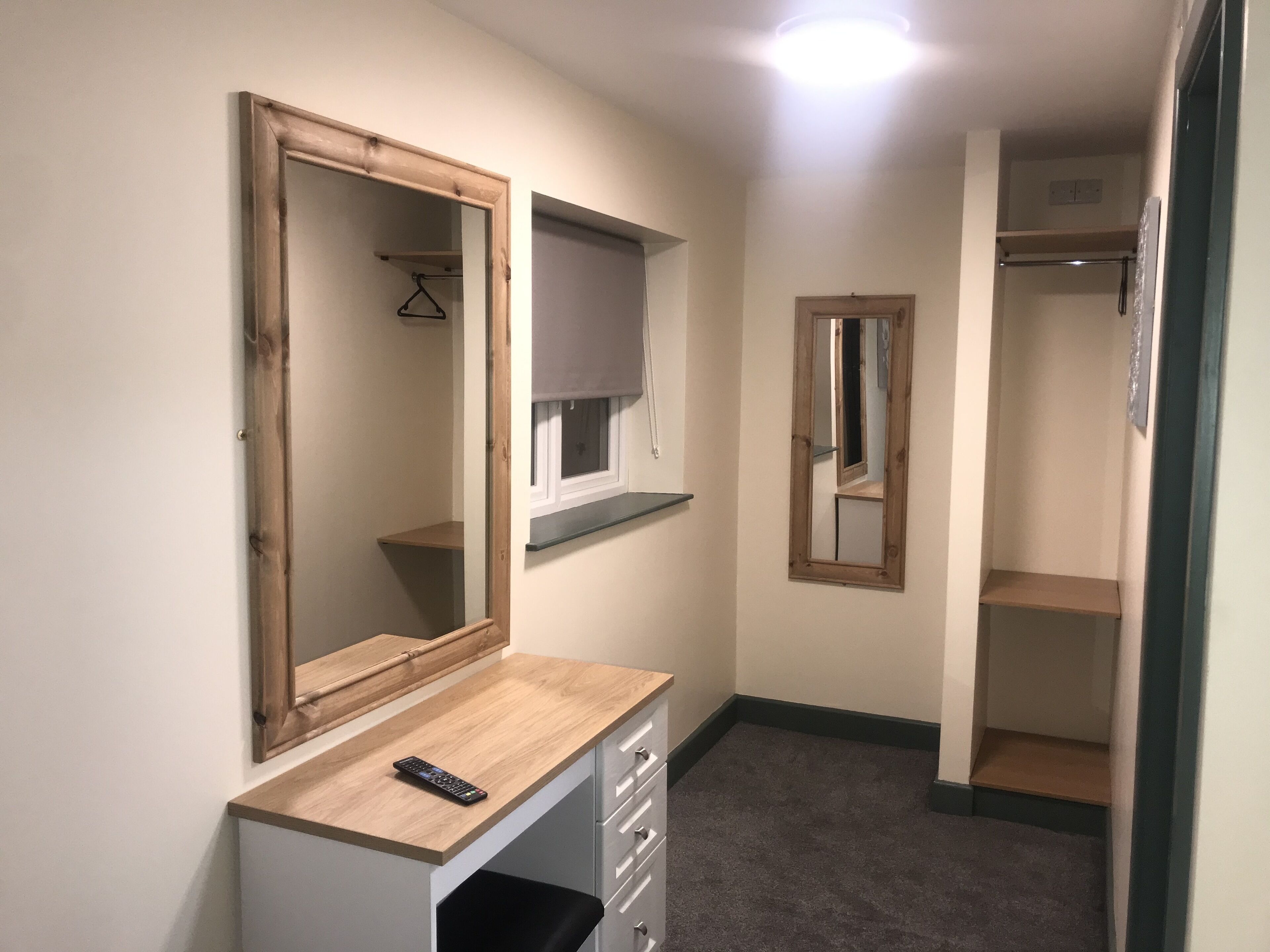 A hallway with a wooden desk, a mirror, and a coat rack.