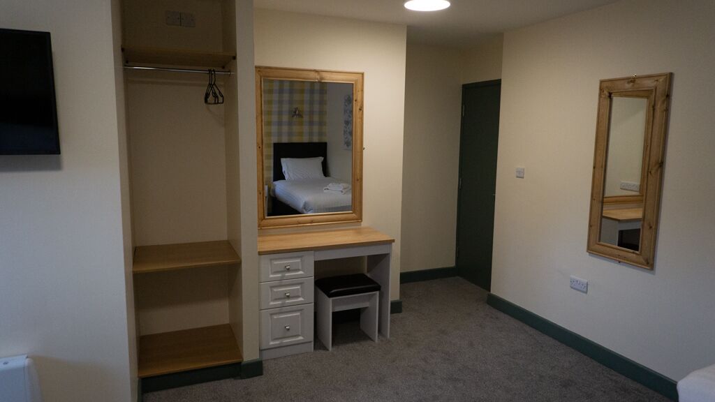 Une chambre avec un bureau en bois, un lit doté d’une tête de lit à carreaux et un miroir au mur.