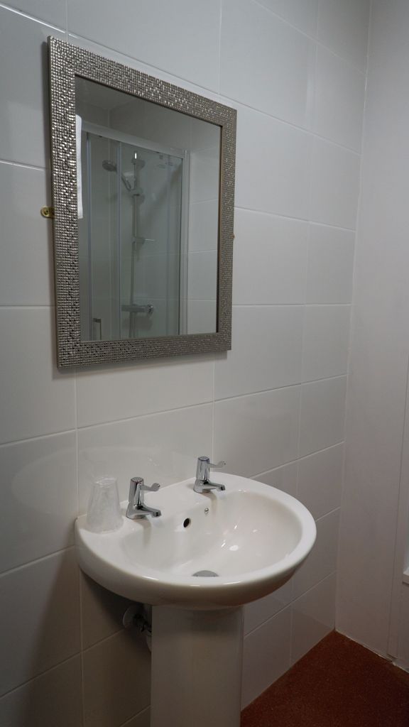 A bathroom with a white sink, a mirror with a textured frame, and a shower visible through the glass door.