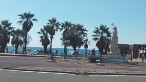 Eine Uferpromenade mit Palmen, einer Statue und Blick auf das Meer.