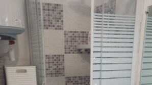 Ein Badezimmer mit Toilette, einer Dusche mit Glastür und gefliesten Wänden.