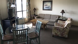 A living room with a sofa, armchair, coffee table, and a dining table with chairs. There is a ceiling fan, a painting on the wall, and a TV on a stand. - Villa with Great Ocean View (Atlantic Beach)