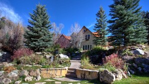 A house surrounded by large evergreen trees and a stone pathway leading to the entrance. - STONEHILL LODGE, SWIM, HIKE, SECLUSION, LUXURY (Midway)