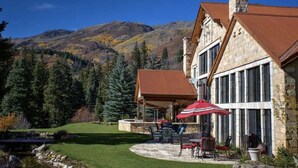 A stone building with a covered patio and outdoor seating area, surrounded by a mountainous landscape and a small pond. - STONEHILL LODGE, SWIM, HIKE, SECLUSION, LUXURY (Midway)