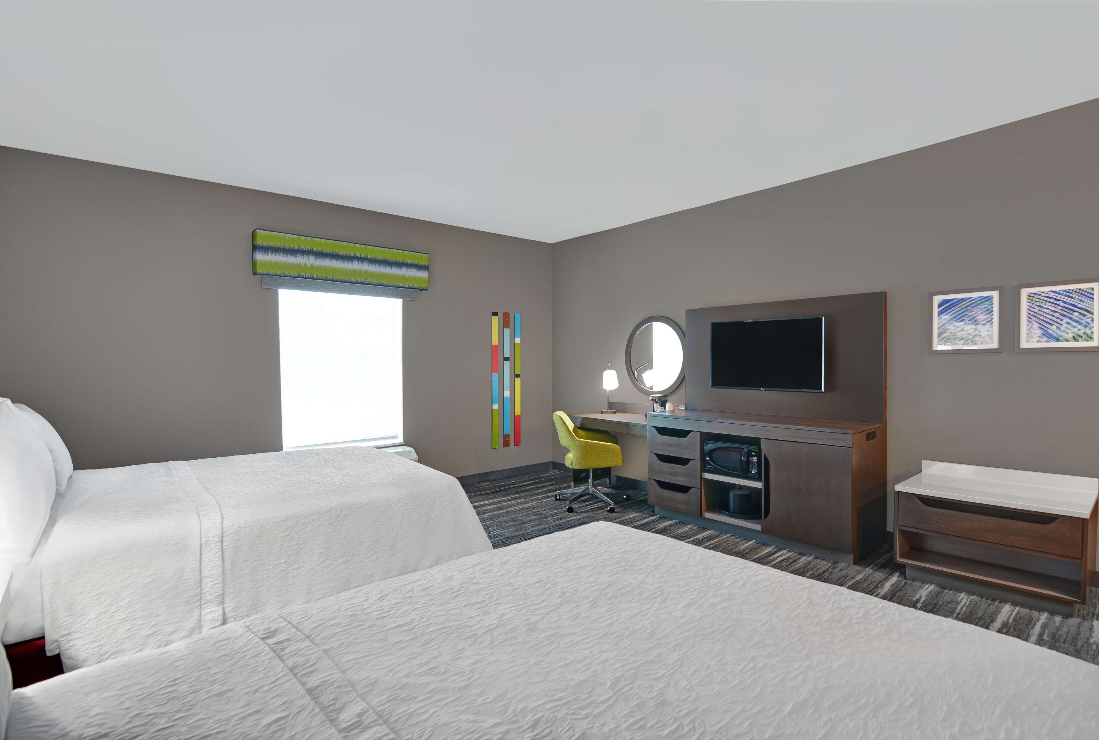 Habitación de hotel con dos camas, un escritorio con silla, televisión y una obra de arte en la pared.